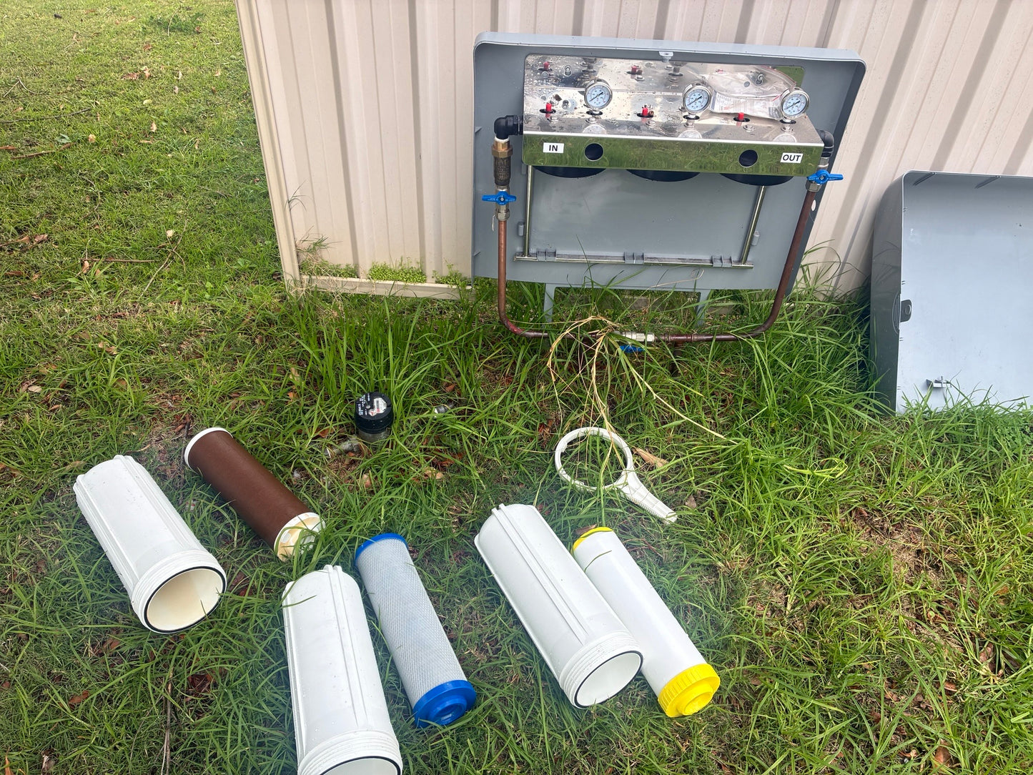 A whole-home filter housing opened for service with used cartridges laid out, including a heavily discoloured sediment cartridge
