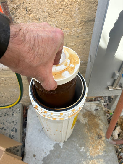 A heavily fouled brown sediment cartridge being lifted out of its housing during a ProperWater filter change