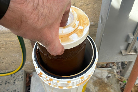A heavily fouled brown sediment cartridge being lifted out of its housing during a ProperWater filter change